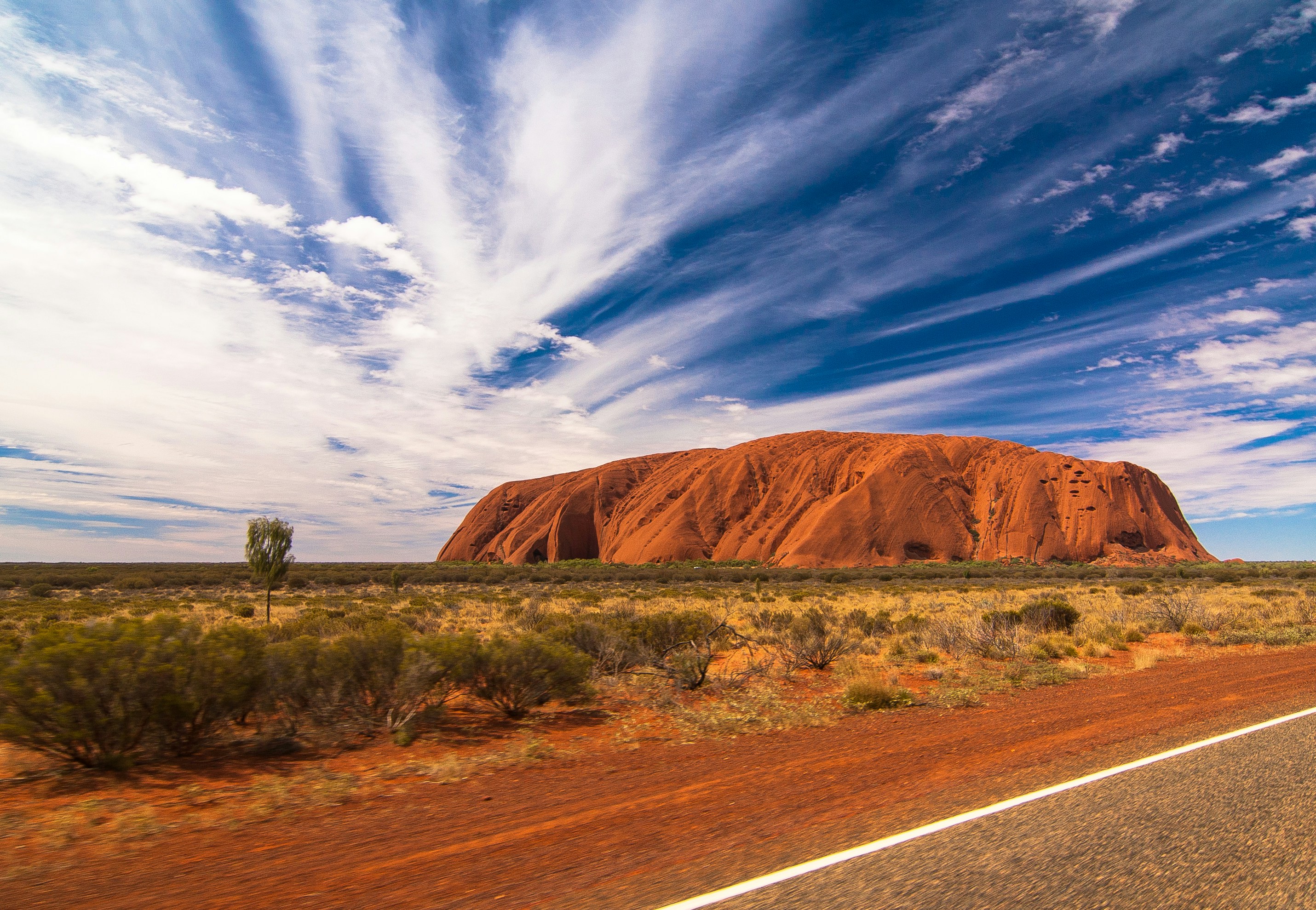 Uluru towers over the Australian Outback in Northern Territory, its red sandstone glowing beneath streaking clouds